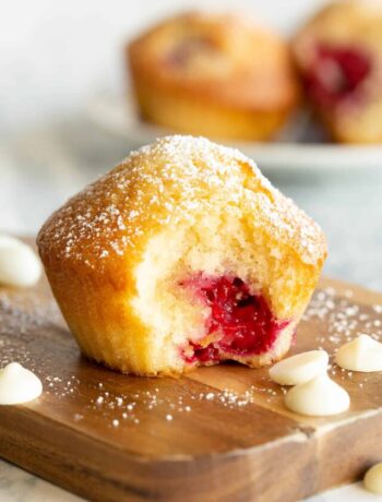 A raspberry muffin sits on a wooden board with a bite taken out.