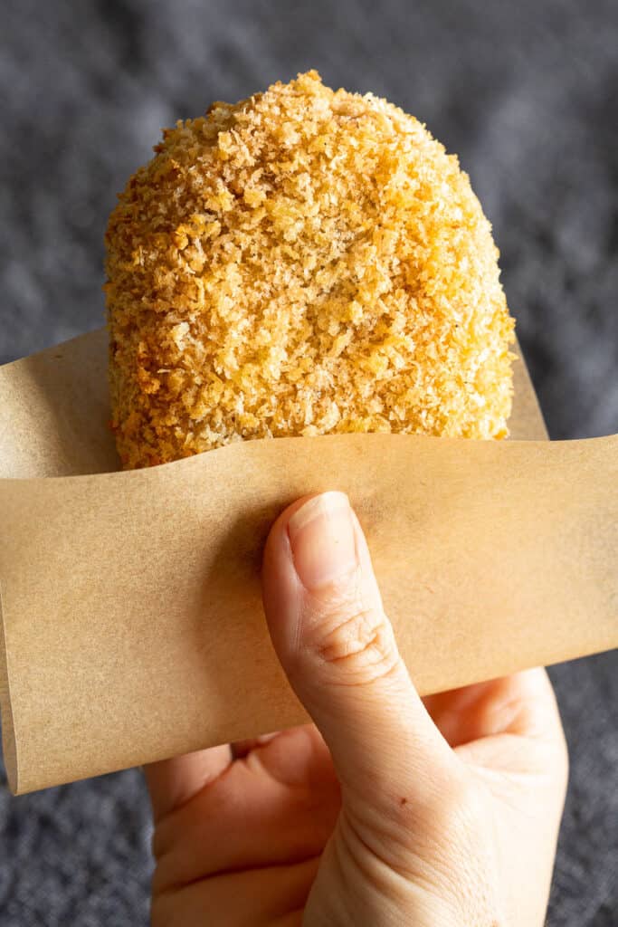 A hand holds a crispy Japanese style meat and potato croquette.