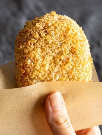 A korokke is held in baking paper with a hand.