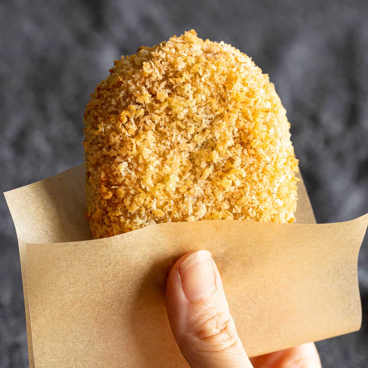 A korokke is held in baking paper with a hand.