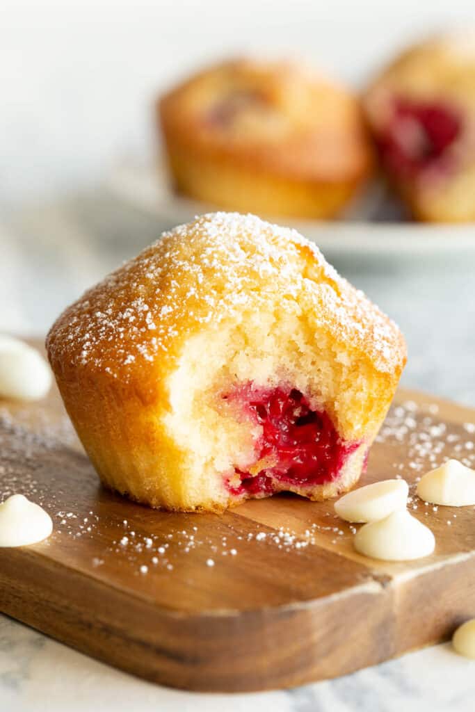 A raspberry muffin sits on a wooden board with a bite taken out.