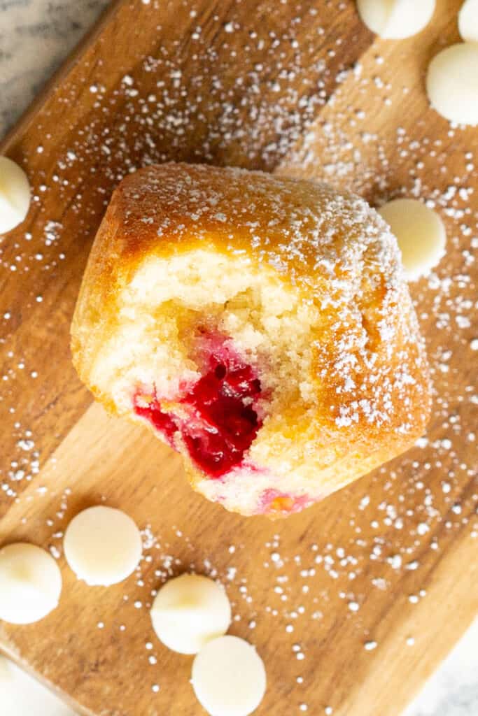 A raspberry muffin is surrounded by white chocolate chips and a sprinkling of iing sugar.