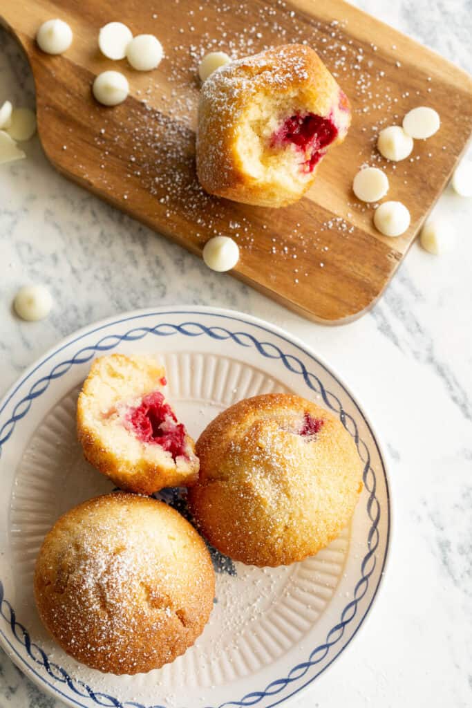 Raspberry muffins are presented on a small plate and wooden board with a sprinkle of white choc chips.