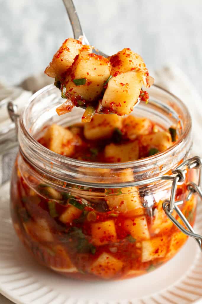 A spoon holds cubed radish kimchi, covered in spices and spring onion.