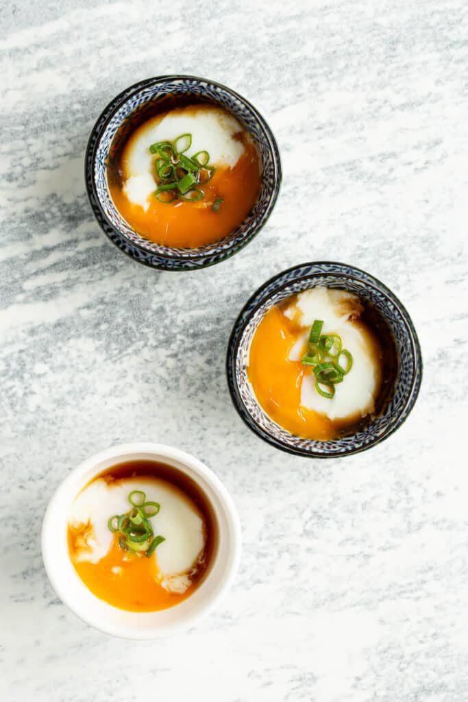 Onsen eggs in small bowls with broken yolks, ready to eat.