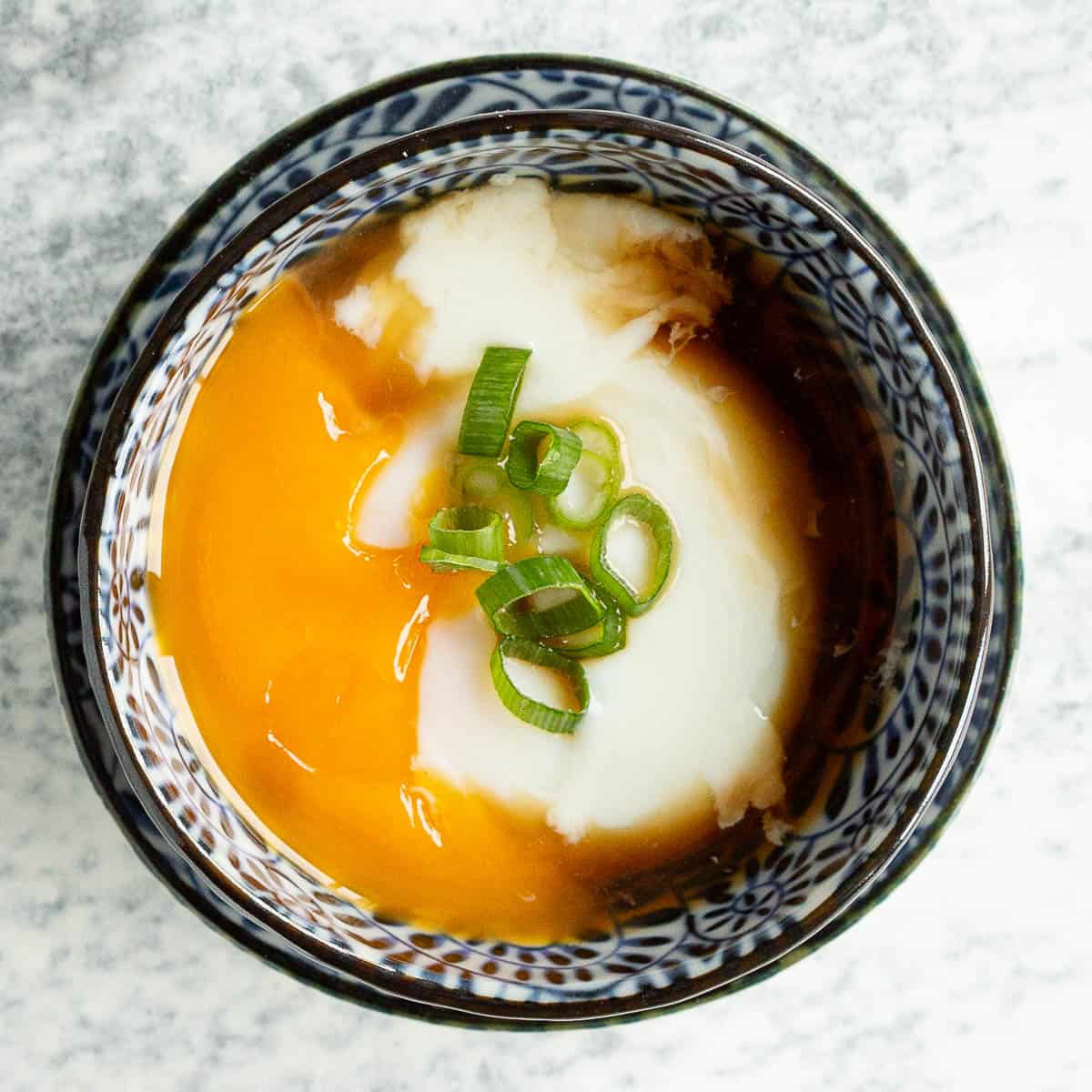 Onsen tamago in a blue bowl with golden yolk oozing out.
