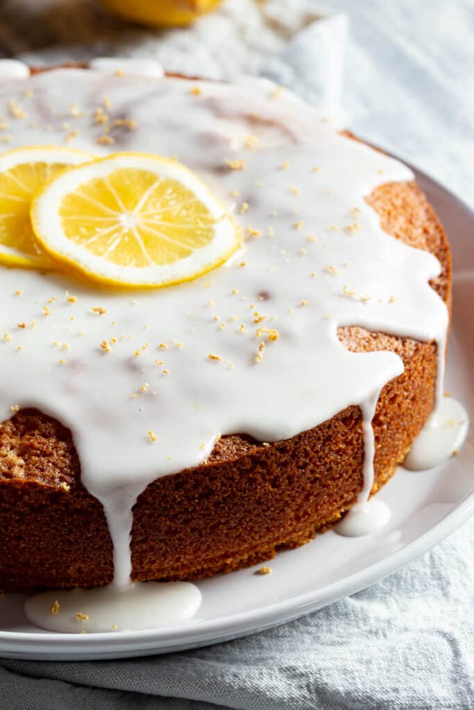 A lemon polenta cake showing the perfect golden edge, topped with a lemon icing drizzle and fresh lemon slices.
