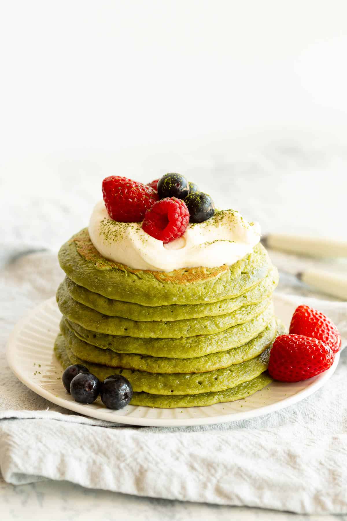 A stack of green pancakes topped with yoghurt and berries.
