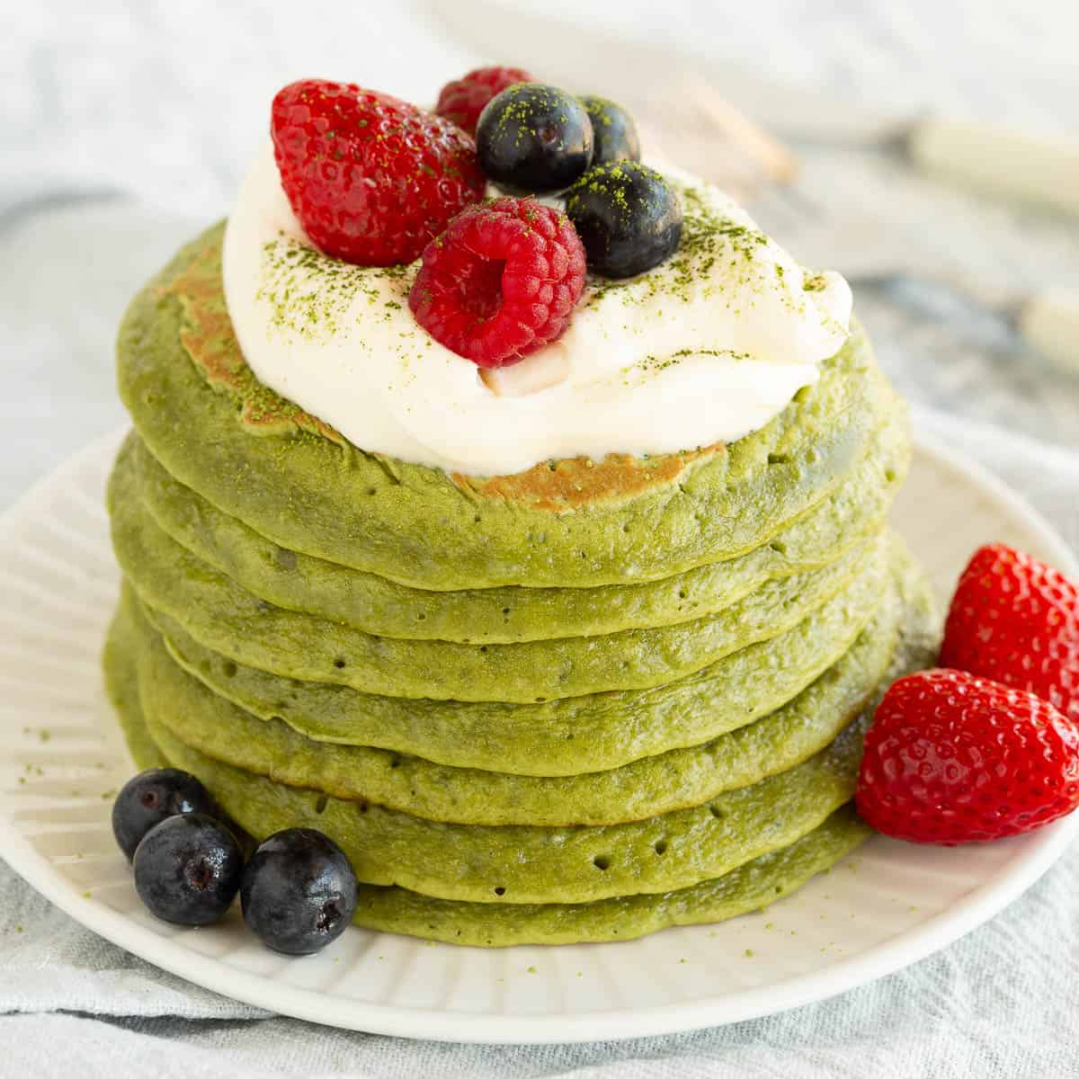 A bright green stack of matcha pancakes with berries and yoghurt on top.