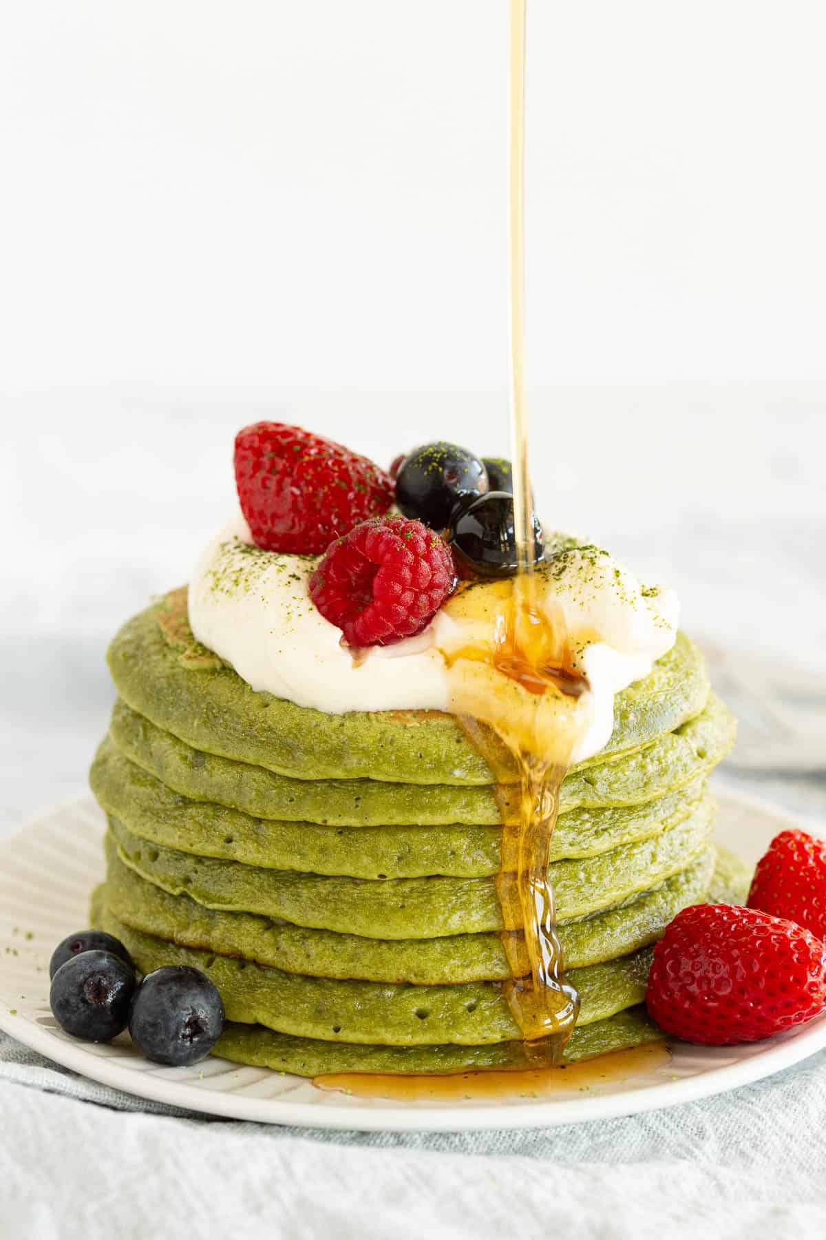 A drizzle of maple syrup slides down the front of a stack of matcha pancakes.