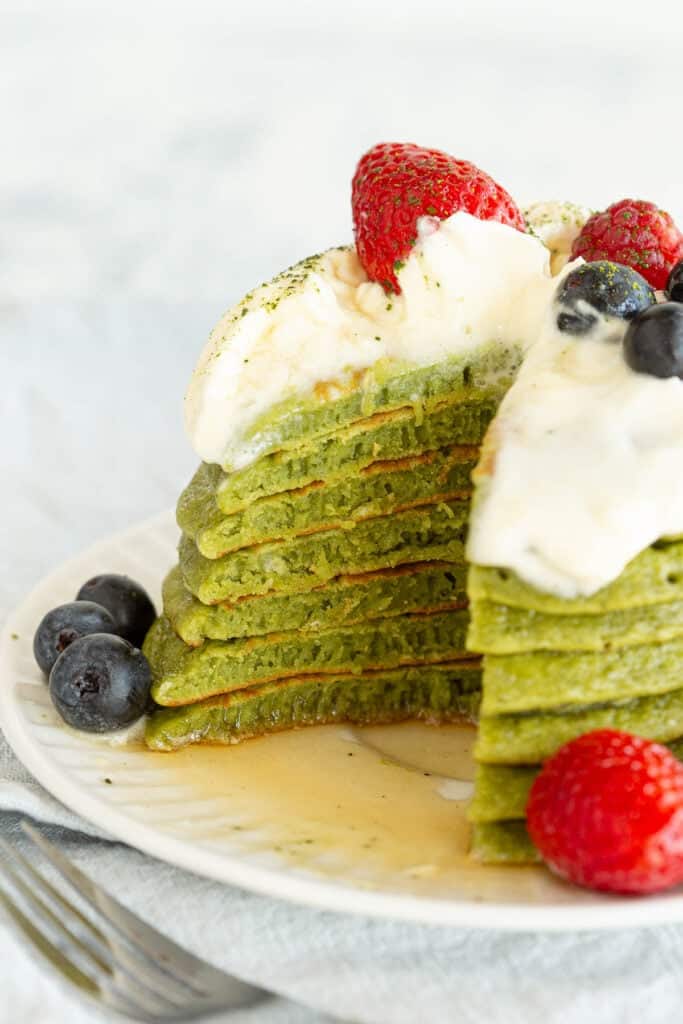 A stack of matcha pancakes shows a portion cut out to see the fluffy individual layers of each pancake.