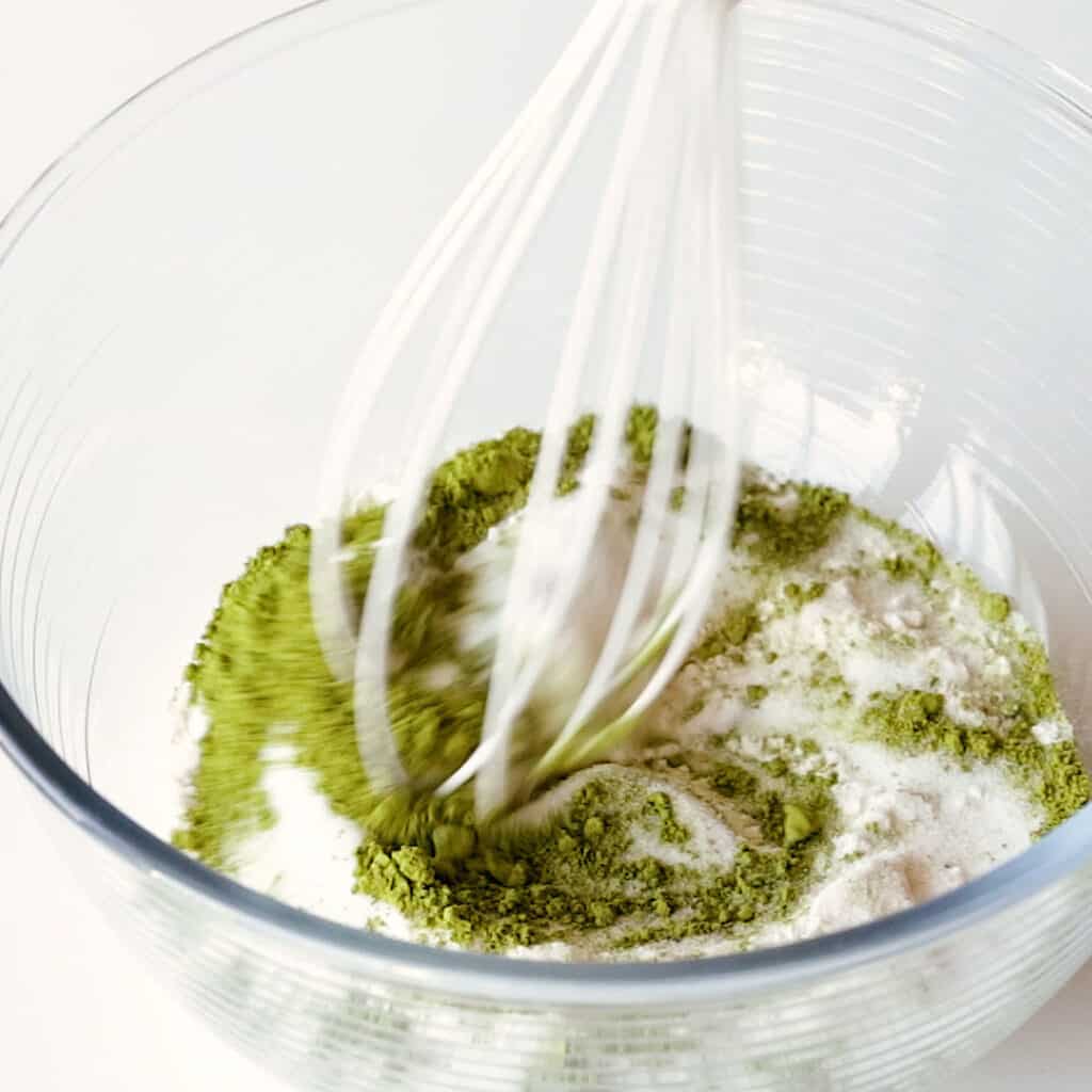 Whisking self raising flour and bright green matcha powder in a bowl.