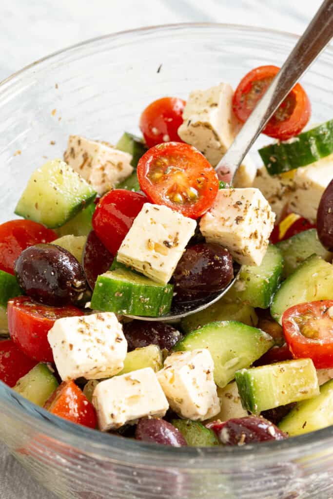 A spoon holds up chopped feta, tomato, olives and cucumber.