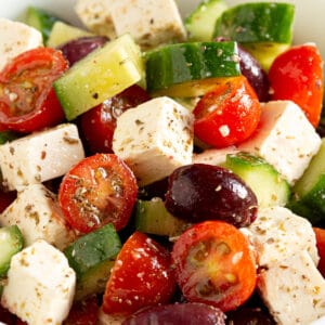 Bright red tomatoes, cucumber, olives and feta in a large white bowl.