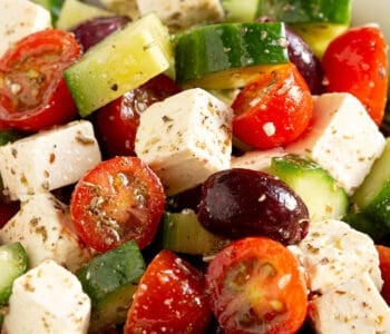 Bright red tomatoes, cucumber, olives and feta in a large white bowl.