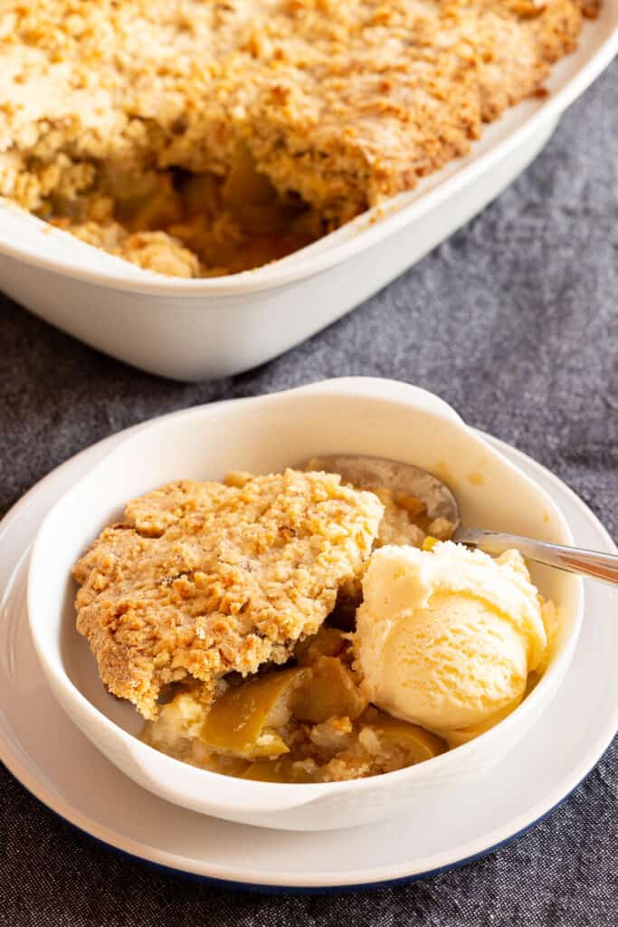 A serving of apple crumble with vanilla ice cream in a small white bowl.