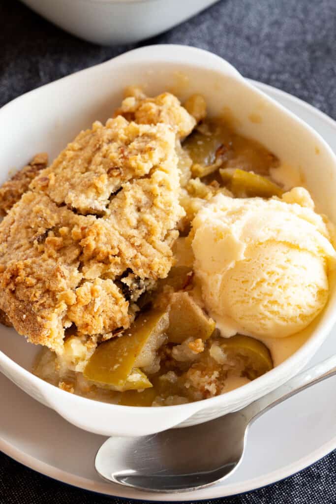 Golden apple crumble with melty vanilla ice-cream in a bowl.