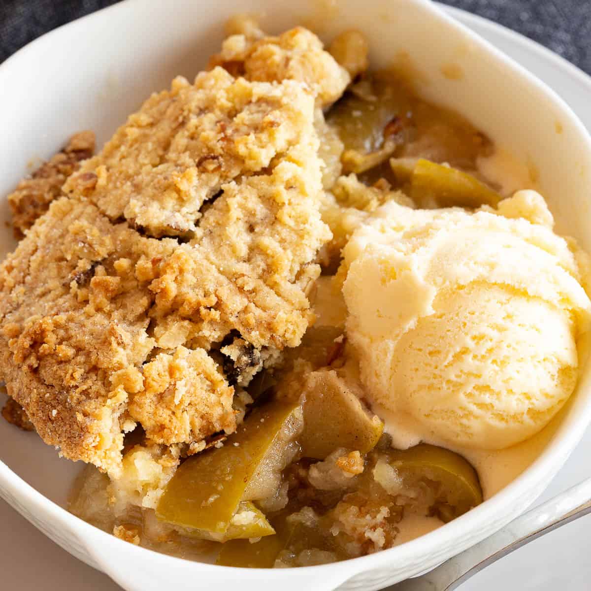 Golden apple crumble with a scoop of ice-cream in a white bowl.