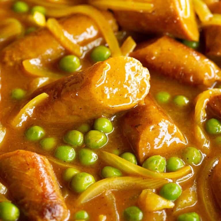 Close up of curried sausages in a pan showing the glossy curry sauce and veggies.