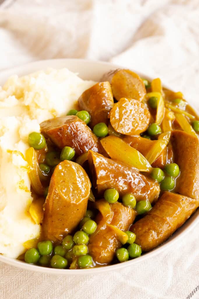 Curried sausages in a white bowl served with mashed potatoes.