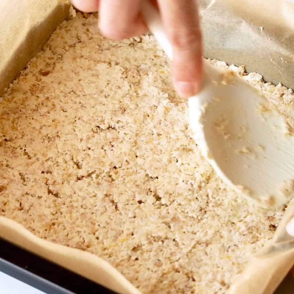 Pressing out the biscuit base into a baking tin.