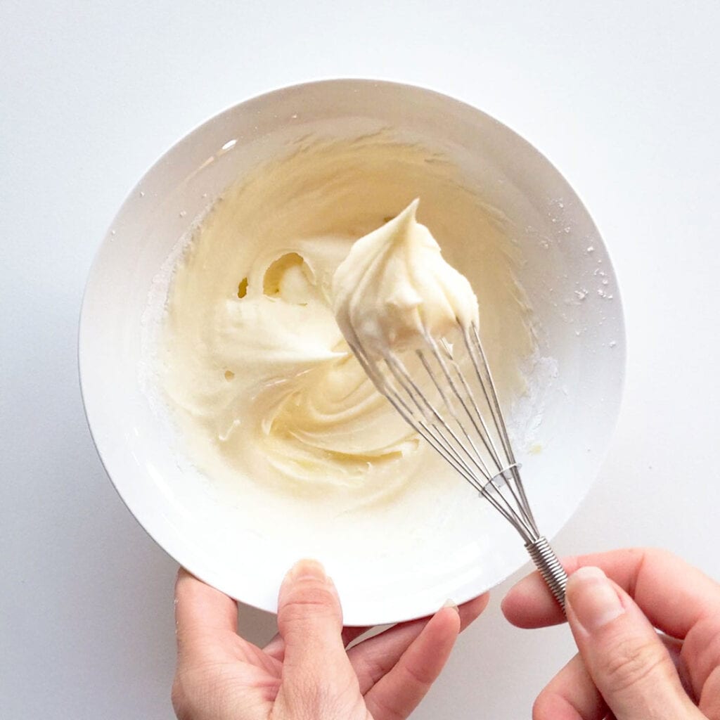 A small whisk shows the creamy texture of the lemon buttercream.