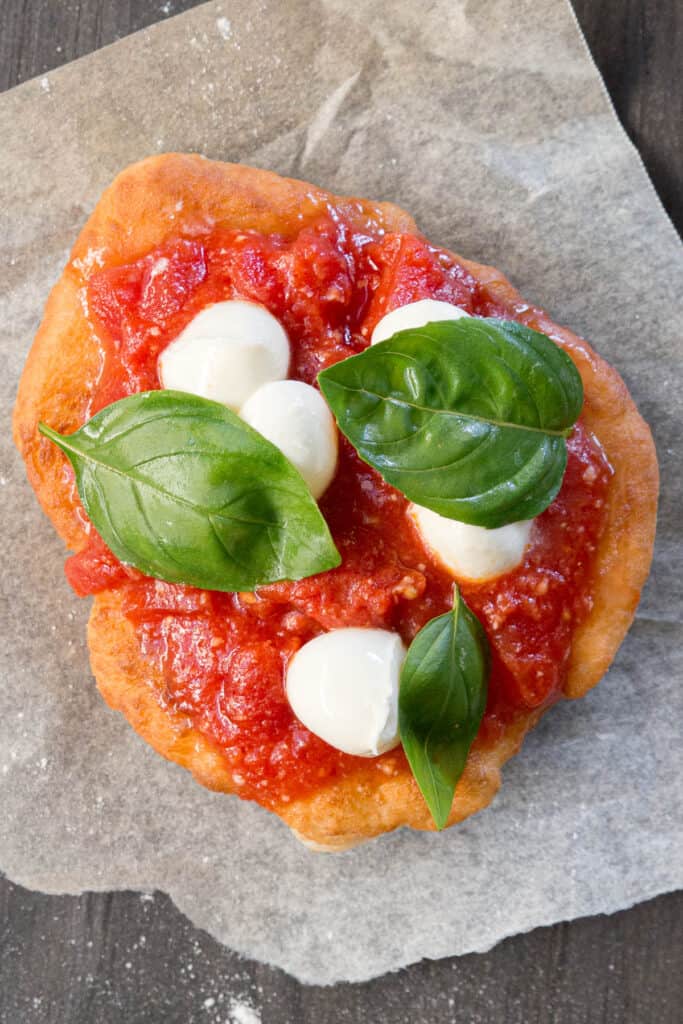 Pizza fritta on a layer of baking paper, topped with pizza sauce bocconcini and bazil.