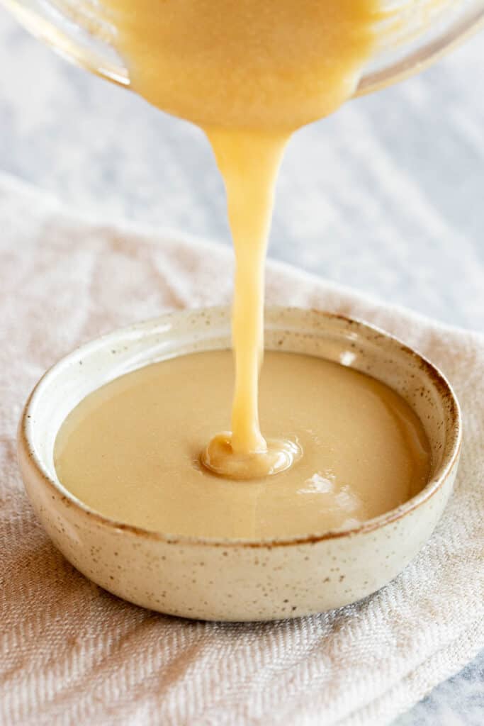 Homemade tahini is poured from the blender into a shallow dish.