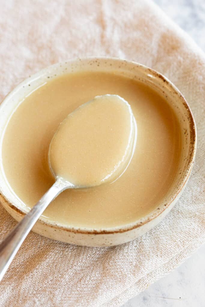 Golden homemade tahini with a spoon in a small dish.