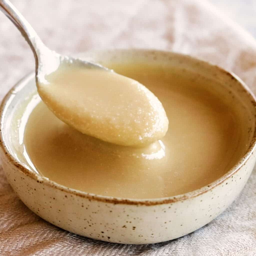 A spoon showing off homemade tahini in a small dish.