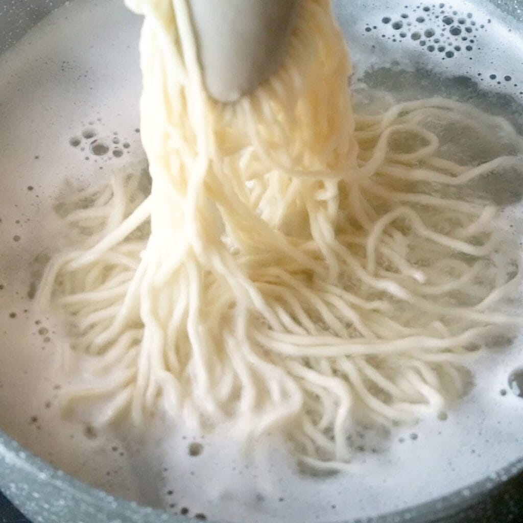 Scooping freshly cooked noodles out of a pot of boiling water.