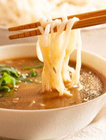 Chopsticks dunk ramen noodles into a creamy brown tsukemen sauce.