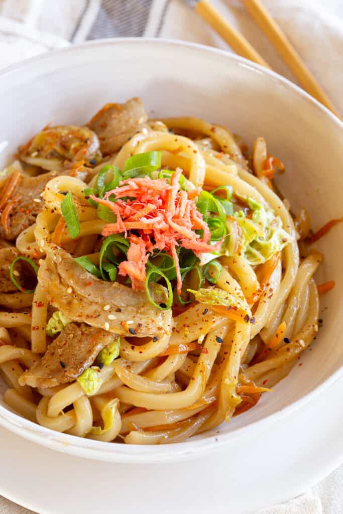 A bowl of yaki udon noodles topped with green onion and red pickled ginger.