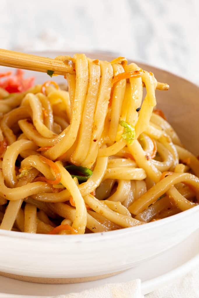 A bowl of yaki udon with some of the noodles held up by chopsticks.