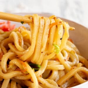 A pair of chopsticks holding several udon noodles above a bowl of yaki udon.