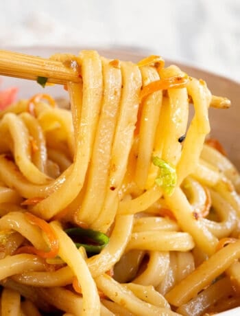A pair of chopsticks holding several udon noodles above a bowl of yaki udon.