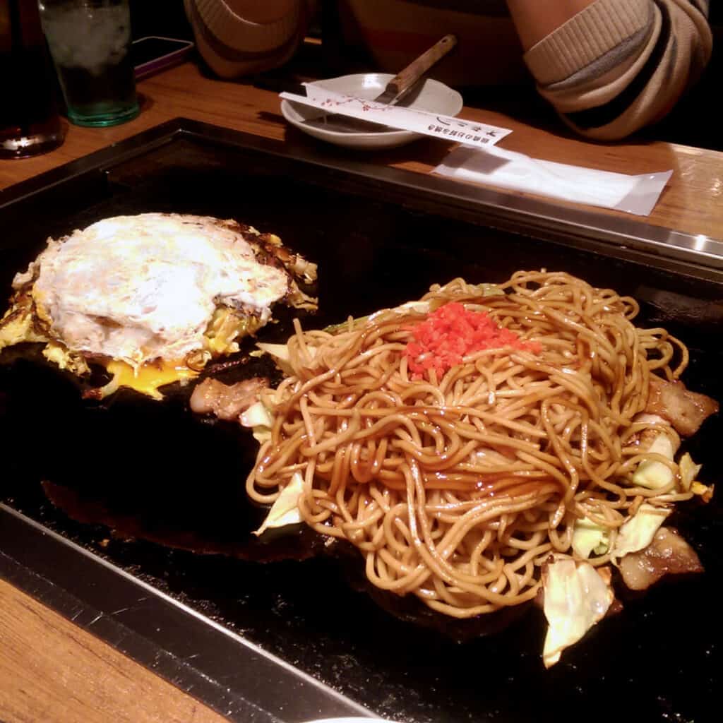 Yakisoba noodles and an okonomiyaki pancake on a teppan hot plate in a Japanese restaurant.