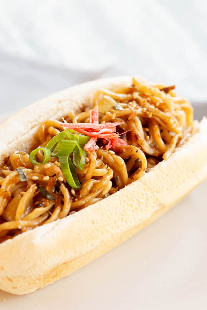 Noodles are neatly stuffed into a hot dog bun and garnished with beni shoga and spring onion.