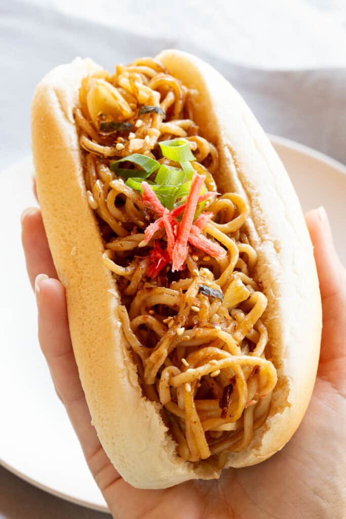 A close up of a yakisoba bun overflowing noodles.