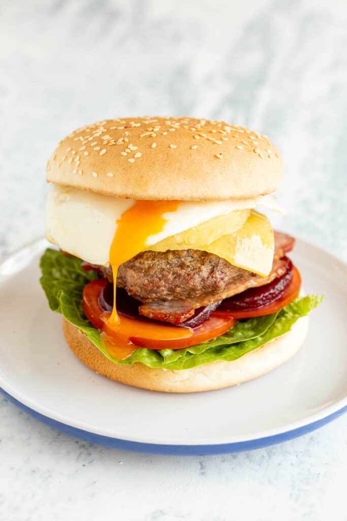 Runny egg drips down the side of an epic Aussie burger on a white plate with blue trim.