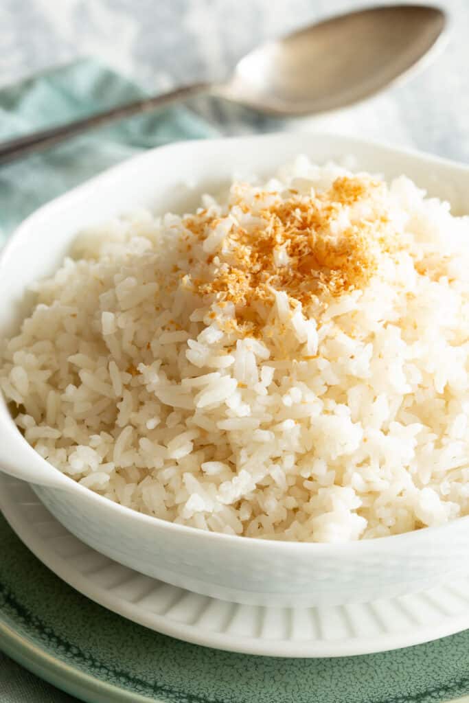 Fluffy white coconut rice in white bowl topped with toasted light brown coconut.