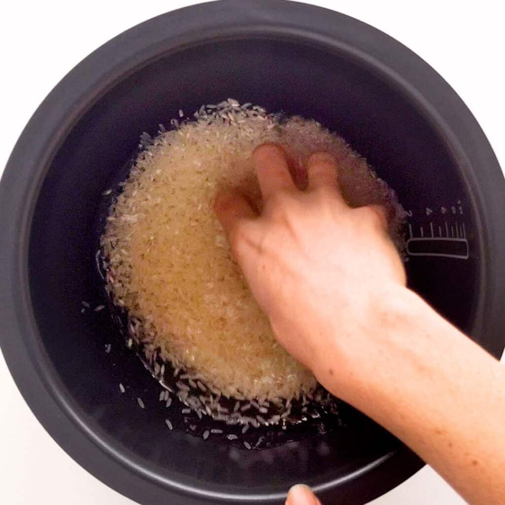 A hand washes rice in a rice cooker pot.