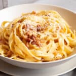 Creamy, golden carbonara in a white bowl on a white plate.