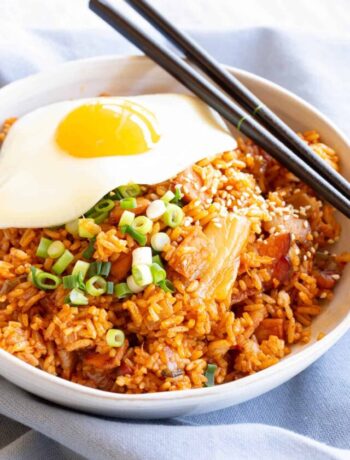 Kimchi fried rice in a white bowl with chopsticks, topped with egg, spring onion and sesame seeds.