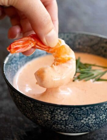 A shrimp is dipped into a bowl of Marie Rose sauce.