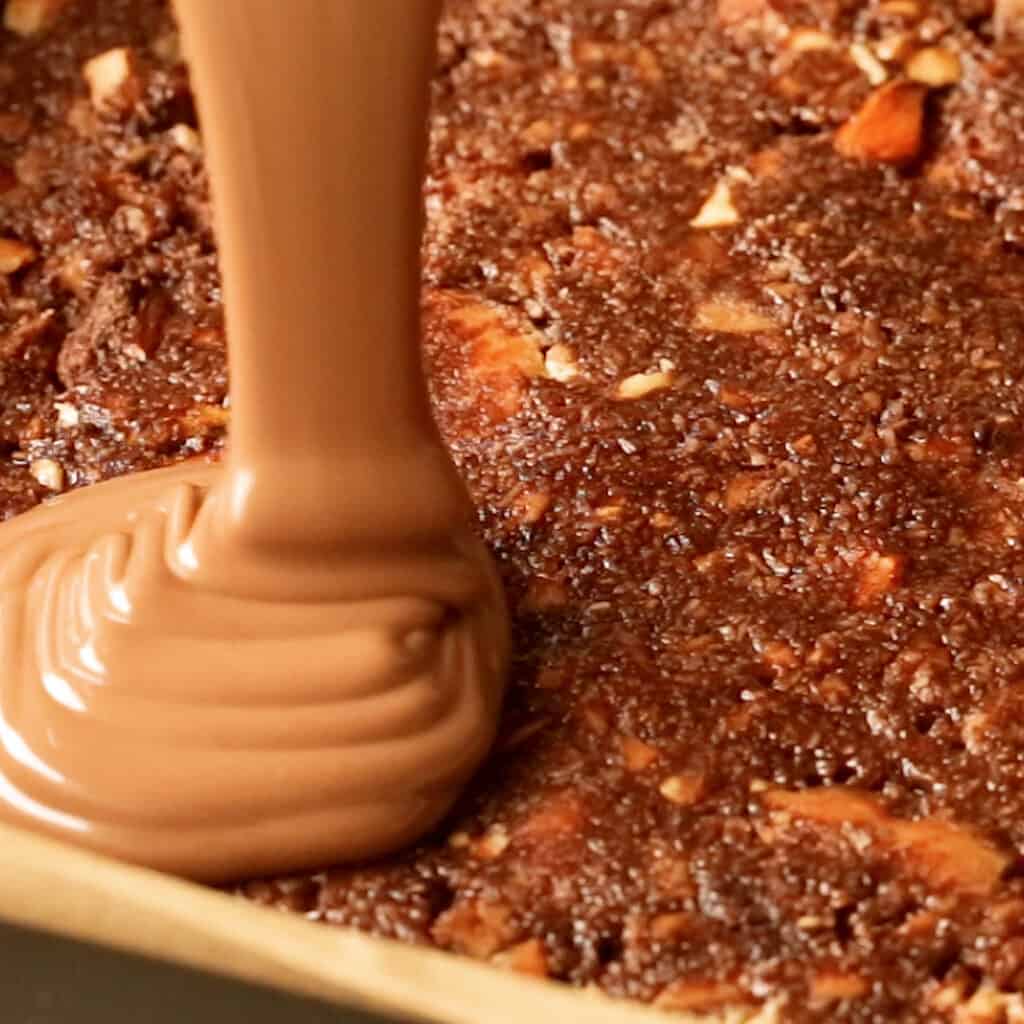 Pouring the melted chocolate over the pressed biscuit base.