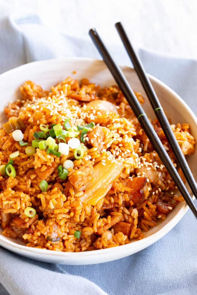 A bowl of kimchi fried rice with a spring onion garnish and chopsticks lying on top.