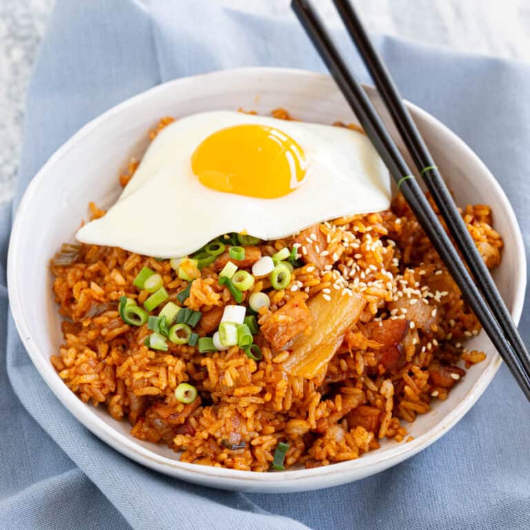 A white bowl on a blue tea towel filled with Korean fried rice and fried egg.