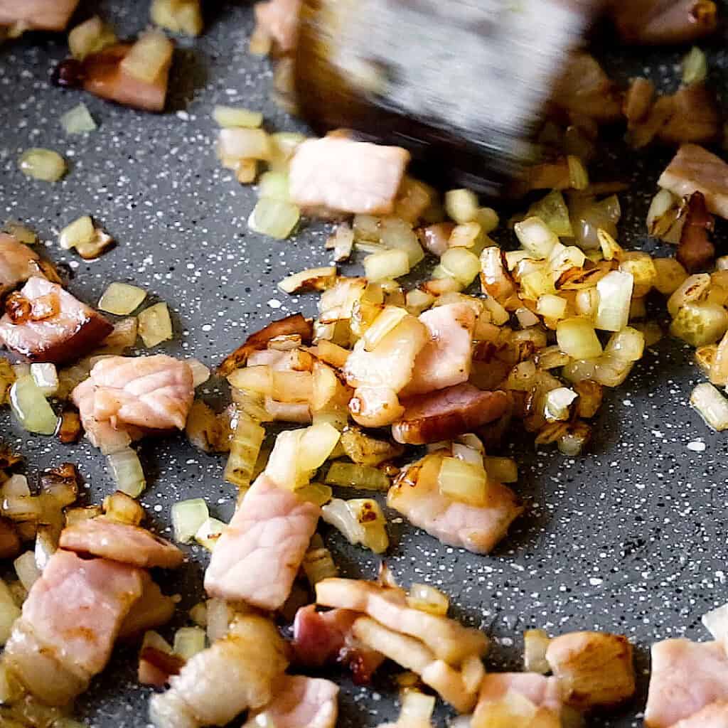 Frying bacon and onion together in a frying pan.