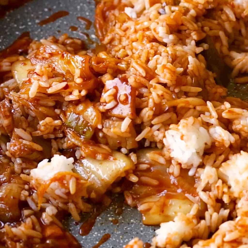 Cooked rice being mixed through the spicy kimchi seasoning.